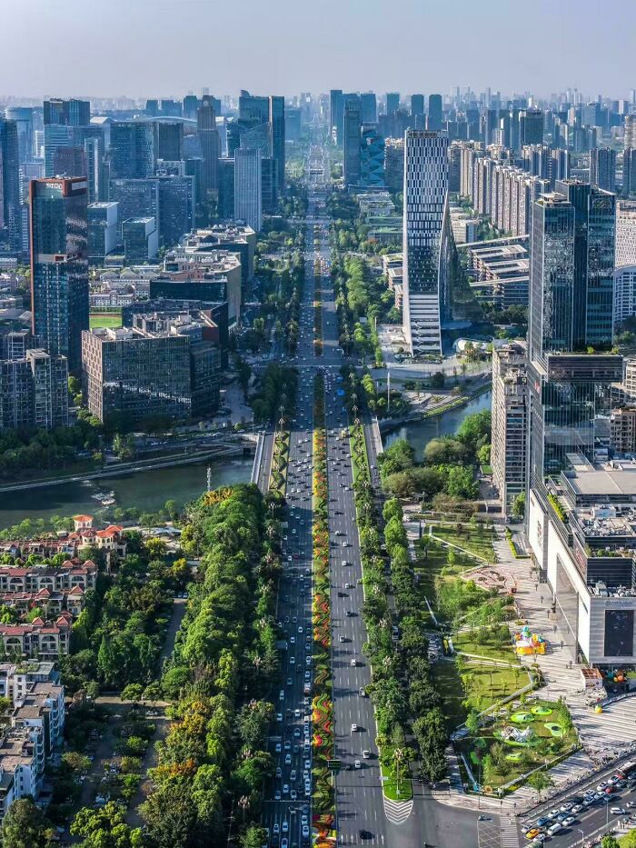 A long, green boulevard stretching through a dense city skyline, representing green best infrastructure.