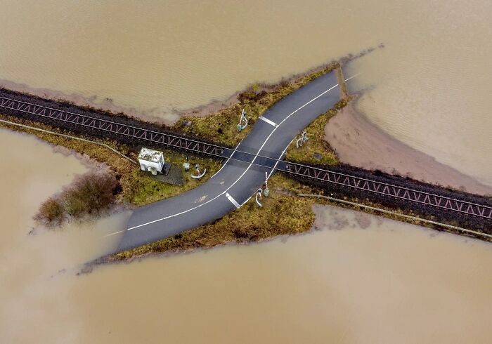 An aerial view of a raised railway and road crossing surrounded by floodwaters, illustrating best infrastructure