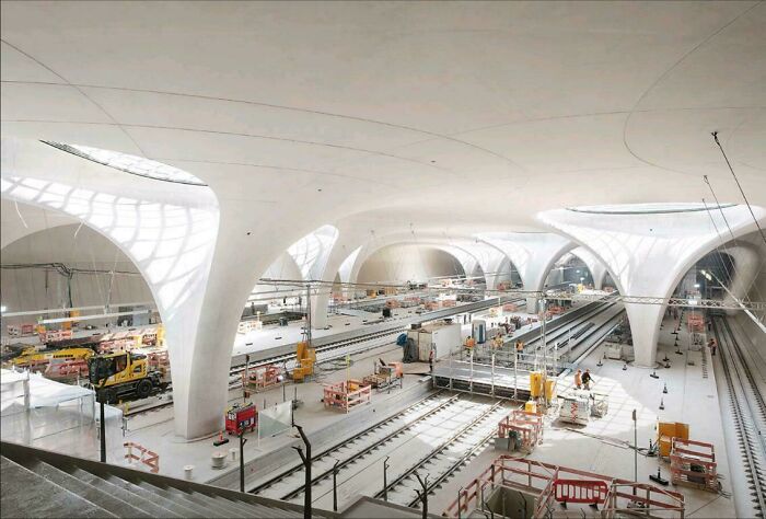 A modern underground train station under construction with large white organic pillars, showing world infrastructure