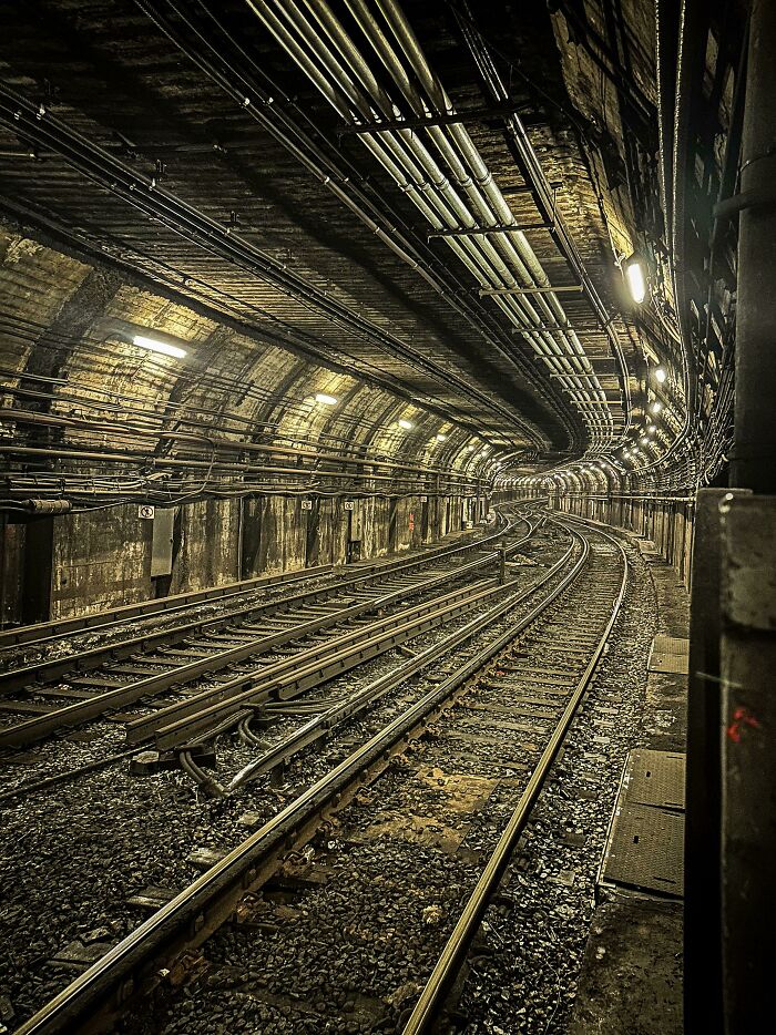 Subway track infrastructure inside a curved underground railway tunnel with overhead pipes