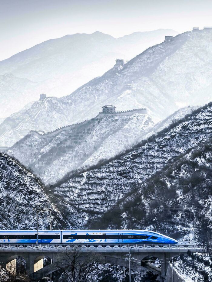 High-speed train infrastructure traversing a bridge below snow-covered mountains