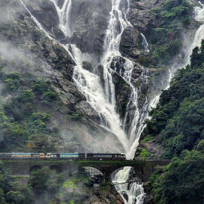 A train passing over a stone arch bridge with a massive waterfall in the background, a beautiful example of infrastructure