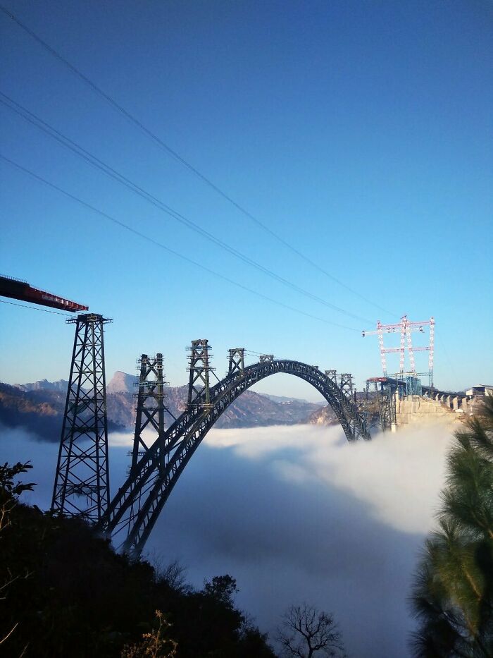 A towering steel arch bridge under construction above the clouds, a feat of world's best infrastructure