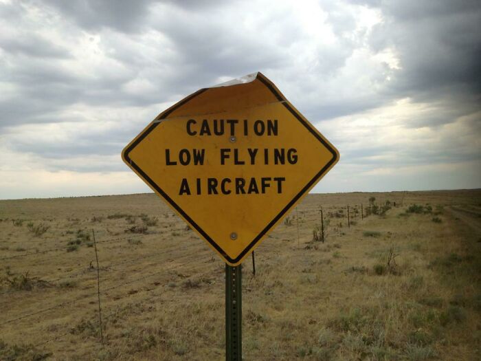 Worn caution sign warning of low flying aircraft in an open field