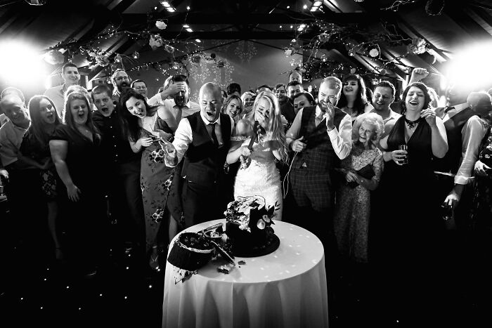 Bride and groom cutting a broken cake at their wedding, surrounded by guests in shock