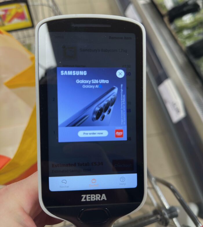 A handheld scanner showing a Samsung ad, a terrible product design that disrupts shopping