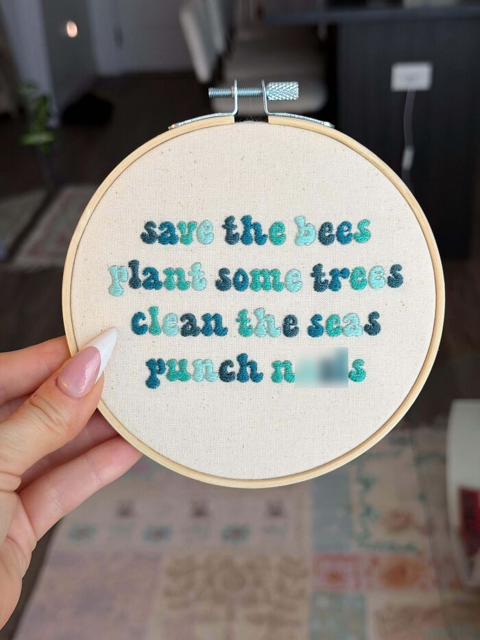 A hand holding an embroidery project hoop with text that reads save the bees, plant some trees