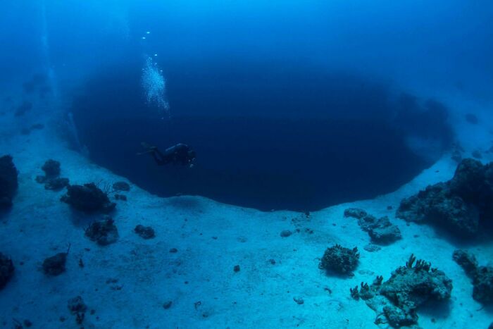 Scuba diver exploring a massive deep blue sinkhole discovered at the bottom of the ocean