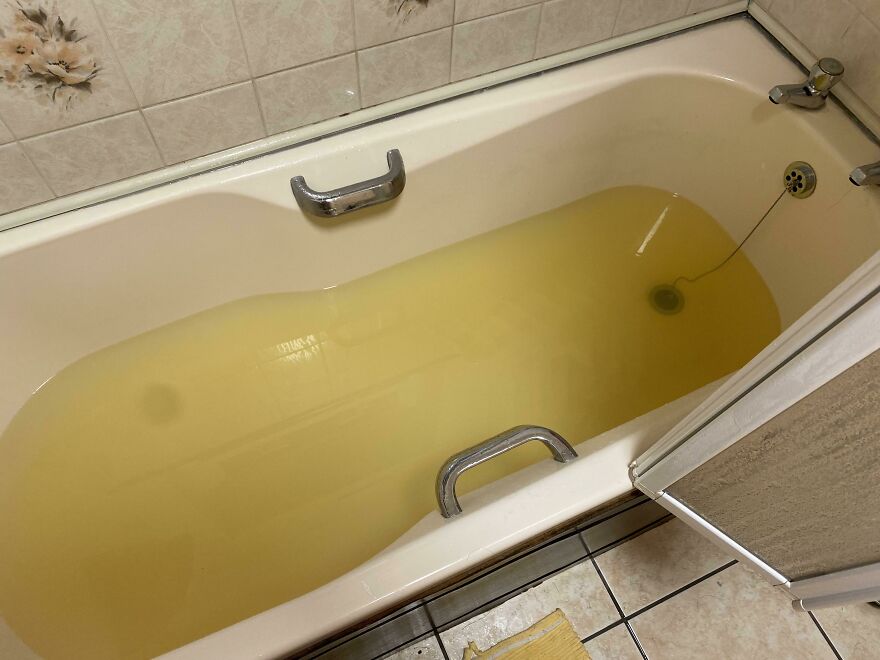 Bathtub filled with murky yellow water and tiled bathroom floor