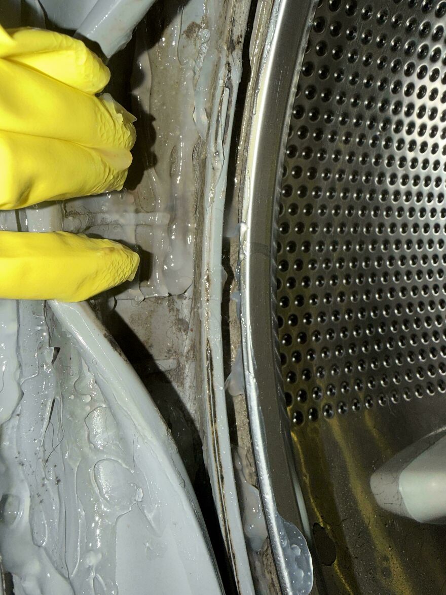 Close-up of dirty washing machine drum with peeling seal and yellow gloves exposing Airbnb fails
