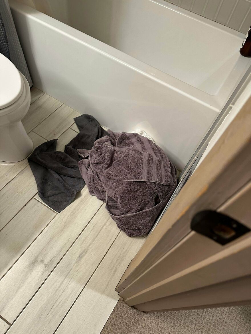 Wet towels on floor by bathtub and toilet showing poor hotel cleaning