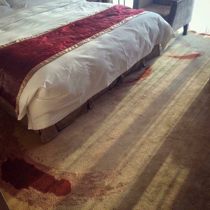 Hotel room carpet stained with a large reddish spill next to the bed