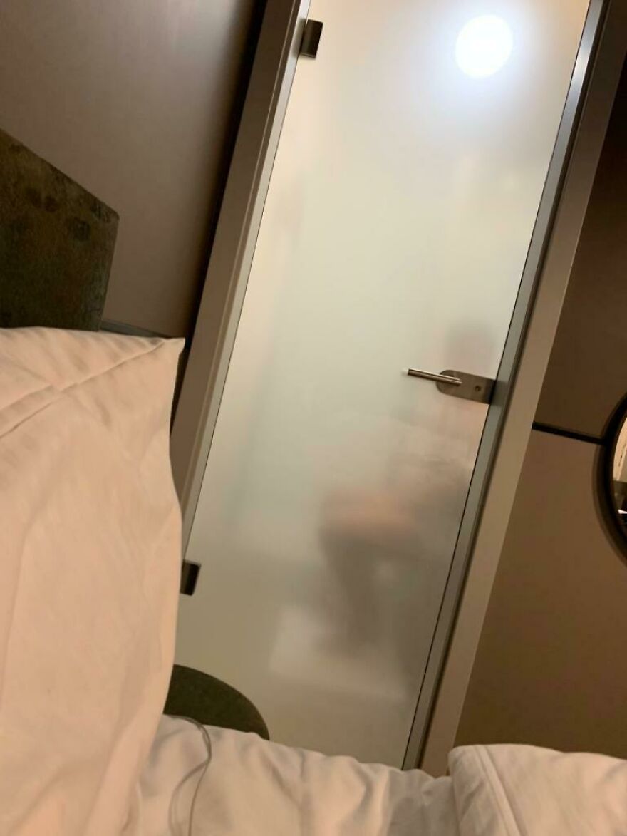 Frosted glass bathroom door revealing a seated person visible from bed