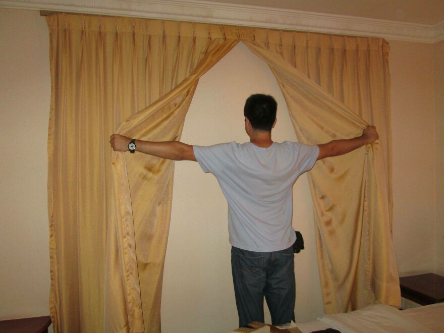 Person opening curtains to reveal a blank wall in hotel room