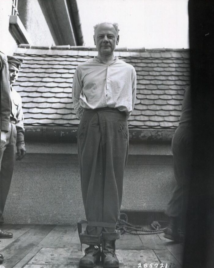 Black and white photo of man with bound legs guarded by soldiers in morbid curiosity stories