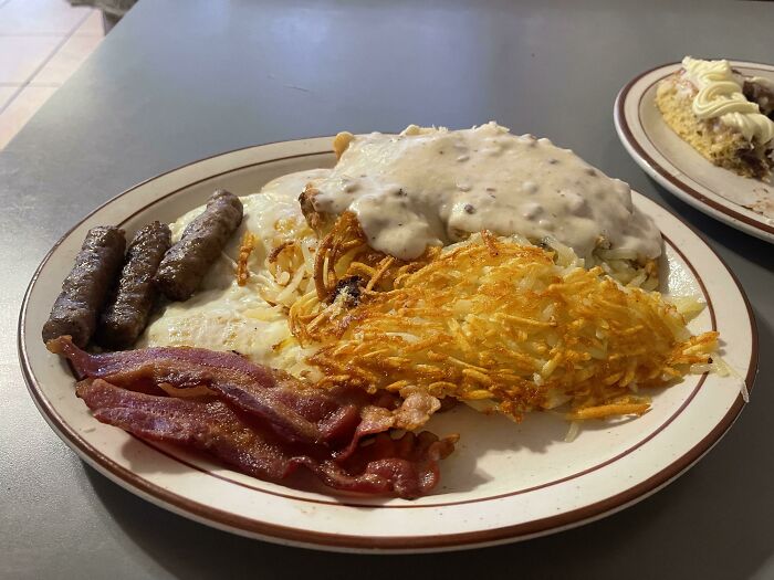 Plate of classic American breakfast with bacon, sausage, hash browns, eggs, and gravy
