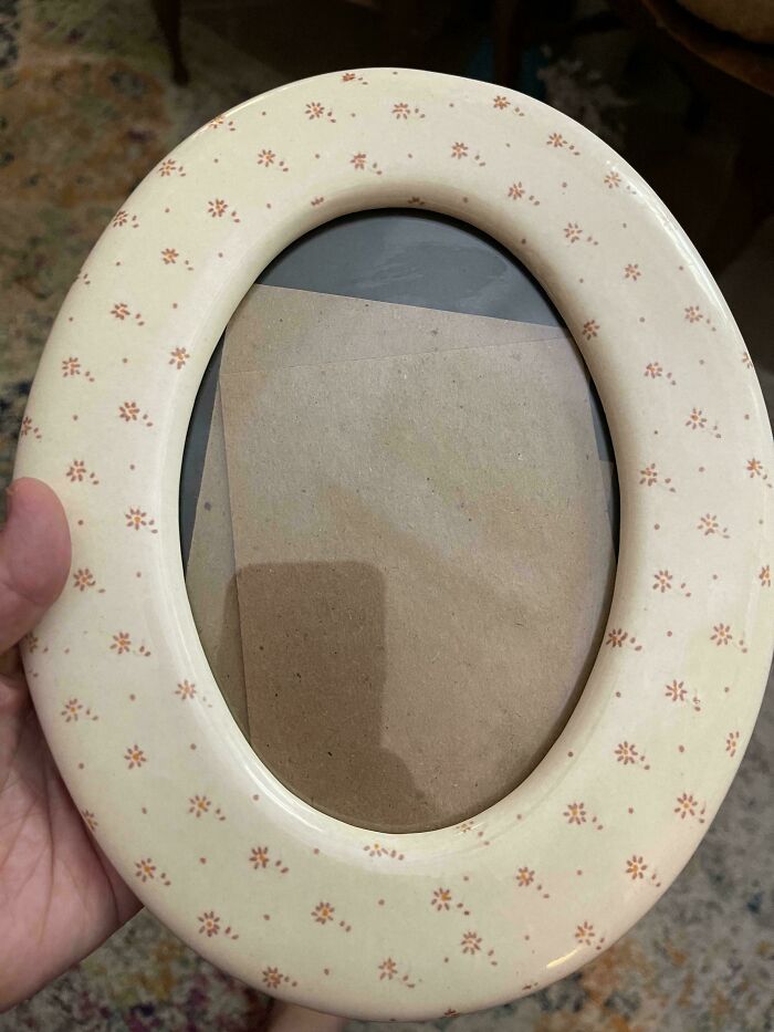 An empty oval ceramic picture frame with a floral pattern found among thrift store finds.