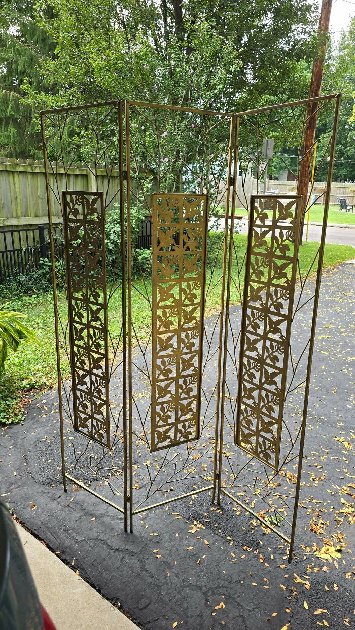 An ornate, gold-painted metal room divider screen standing on a driveway, a rare secondhand find.