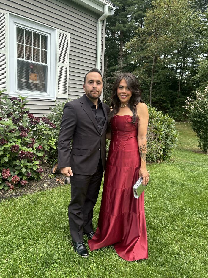 A couple posing outdoors, with the woman wearing a stunning red satin dress, one of many great secondhand finds.