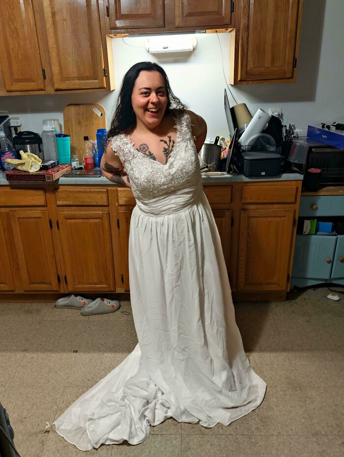 Smiling woman trying on a white lace wedding dress found at a secondhand thrift store.