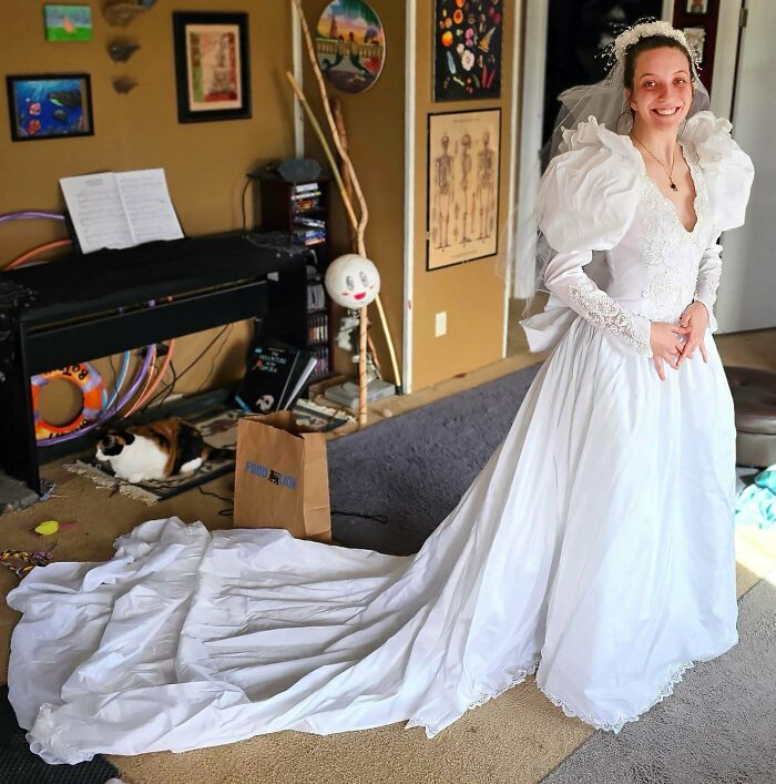 A happy bride trying on a vintage white wedding dress with a long train, found at a thrift store
