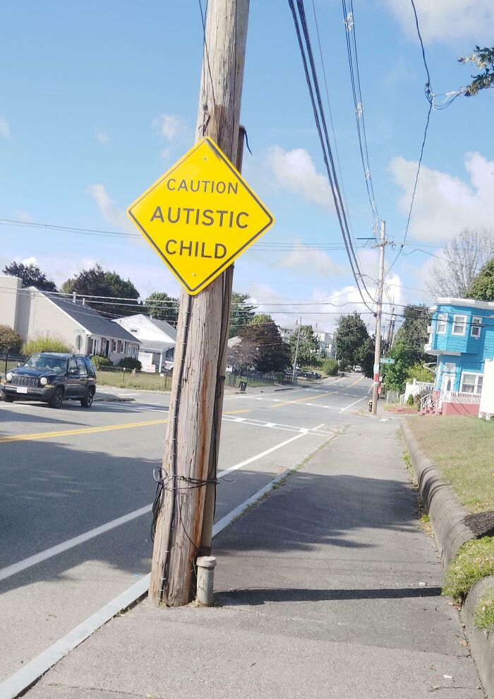 A yellow diamond caution sign on a wooden post saying Autistic Child, which looks like a mistake.