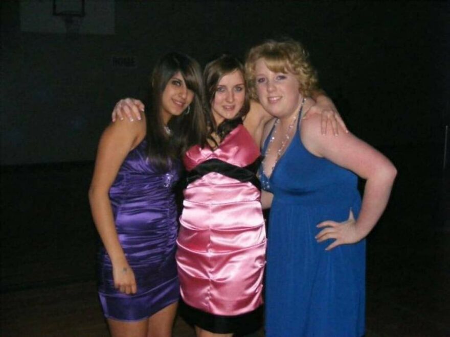 Three teenage girls wearing colorful satin prom dresses in the early 2000s.