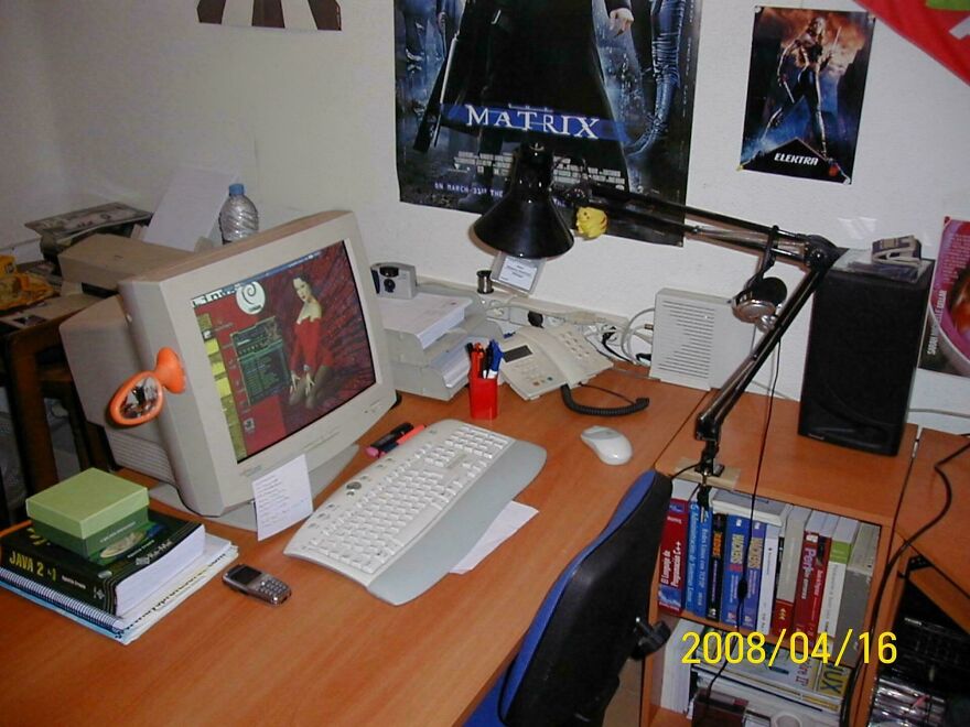 A desk setup featuring a CRT computer monitor, Matrix poster, and tech from the early 2000s.