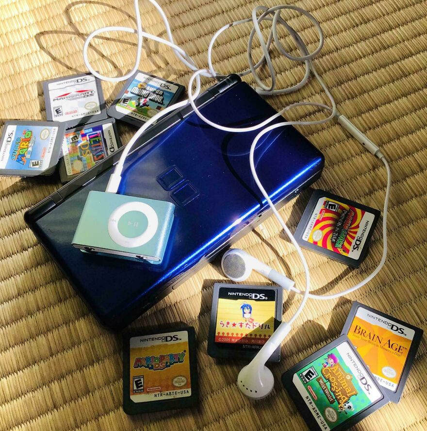 A blue Nintendo DS Lite surrounded by game cartridges and an iPod shuffle, showcasing early 2000s technology