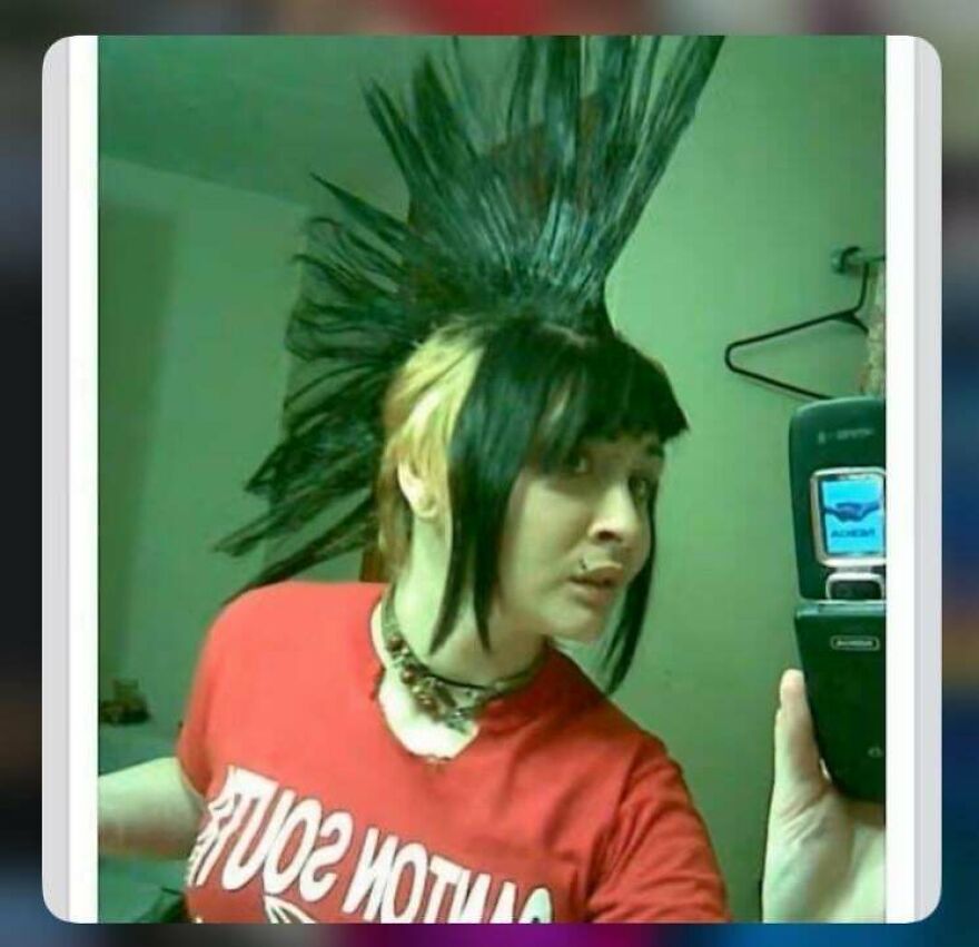 A teenage girl with a massive black and blonde punk mohawk taking a selfie on a flip phone from the early 2000s