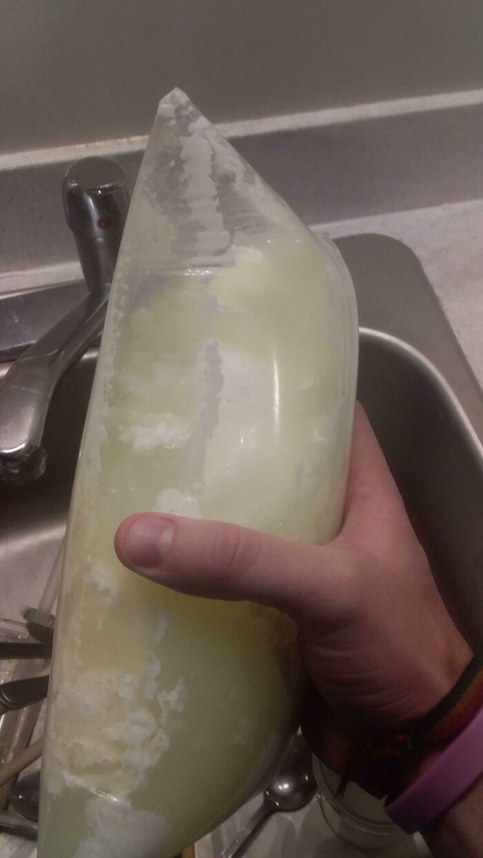 A hand holding a plastic bag containing frozen milk next to a sink, an interesting photo of everyday objects.