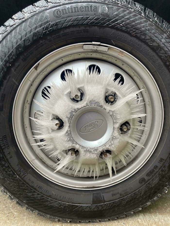 Spiky ice formations radiating outward on a car wheel hubcap, representing cool photos of winter weather effects.
