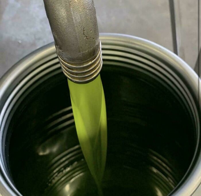 Bright green fluid pouring smoothly from a metal spout into a container, showcasing interesting photos of laminar flow.