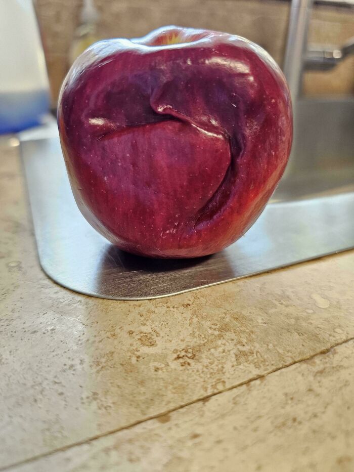 A red apple with a deep wrinkle on its skin, resembling a human ear, depicting cool photos of unique natural shapes.