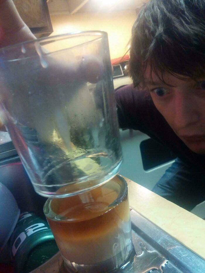A person with wide eyes looking at a glass upside down on another, from interesting and cool photos.