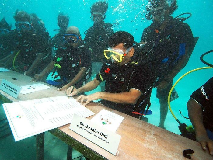 Maldivian cabinet ministers wearing scuba gear and signing documents at an underwater meeting.