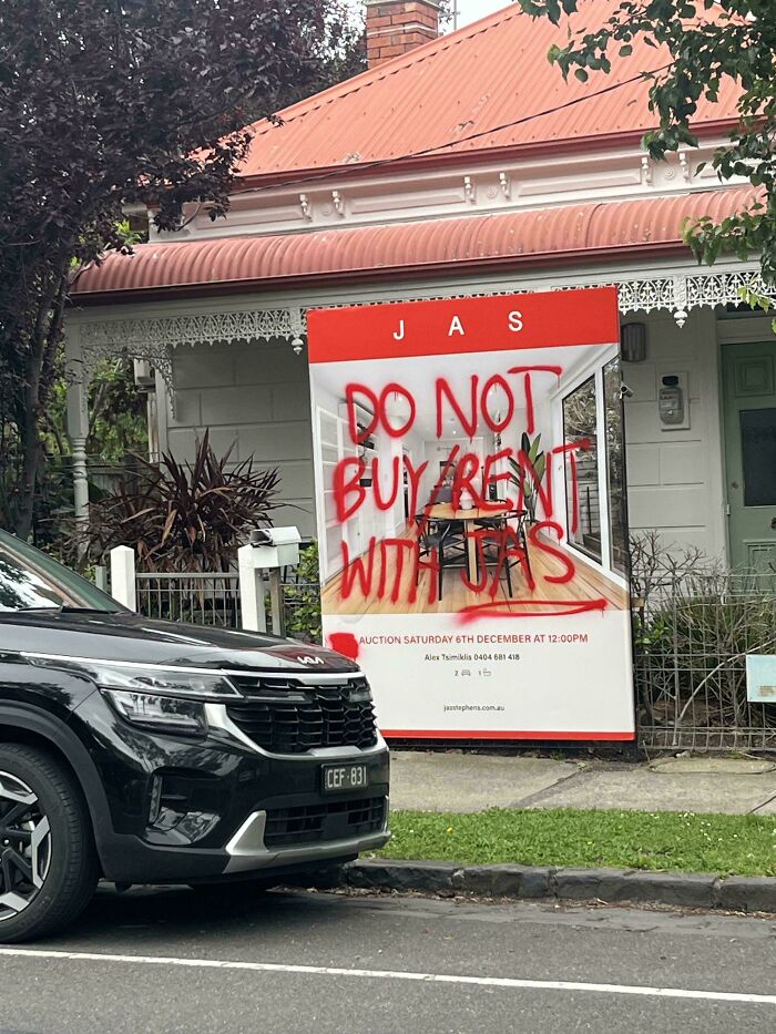 A real estate sign spray-painted with warning graffiti warning against renting and booking with JAS