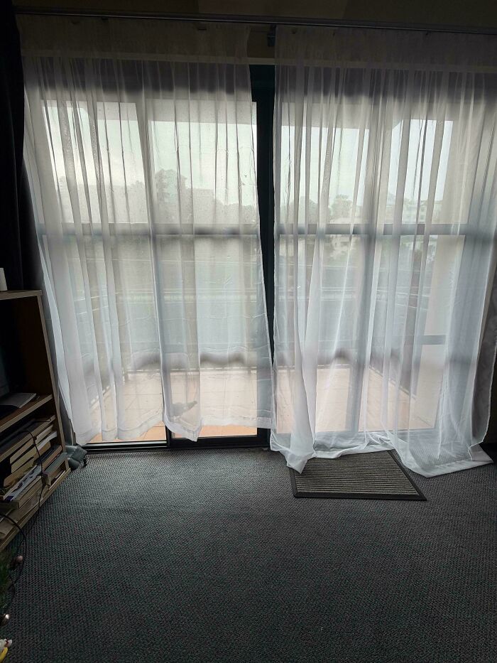 Sheer curtains hanging unevenly on a sliding door in a renting and booking apartment