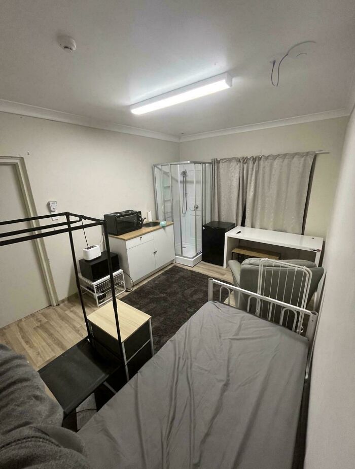 A poorly laid out studio apartment with a bed next to a kitchen and shower, showing a bad renting experience.