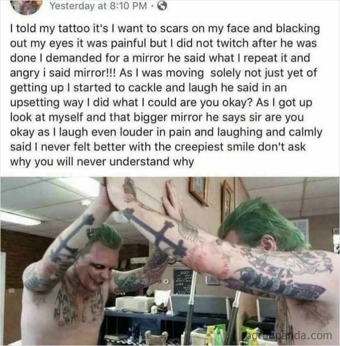 Tattooed man with green hair looking at himself in mirror with creepy smile in tattoo parlor