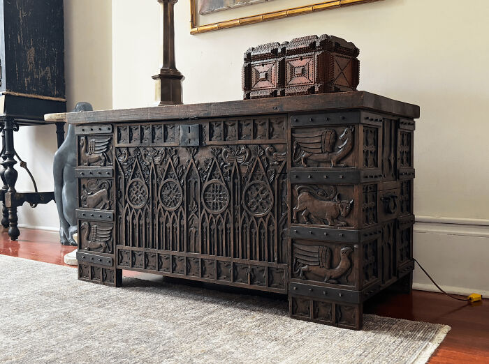 An intricately carved Gothic style wooden chest resting on a rug, showcasing detailed old treasures discovered by antique lovers.