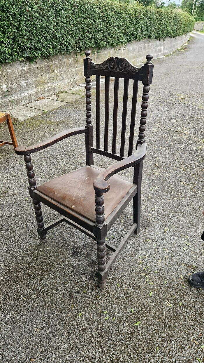 A dark wooden armchair with carved details standing outdoors, a discovery for antique lovers seeking old treasures.