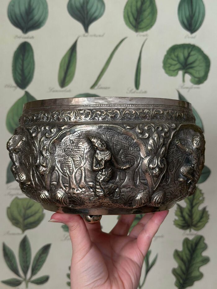 Hand holding an ornate silver bowl with relief carvings of figures and elephants for antique lovers to treasure.