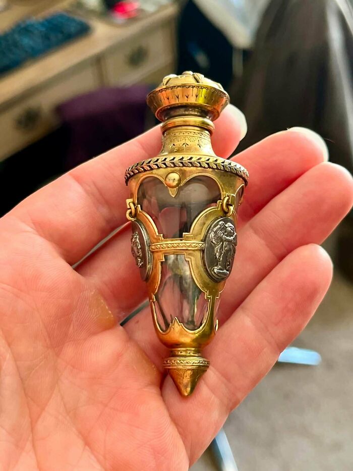 Ornate antique glass and gold perfume phial held in hand, a rare item for antique lovers.