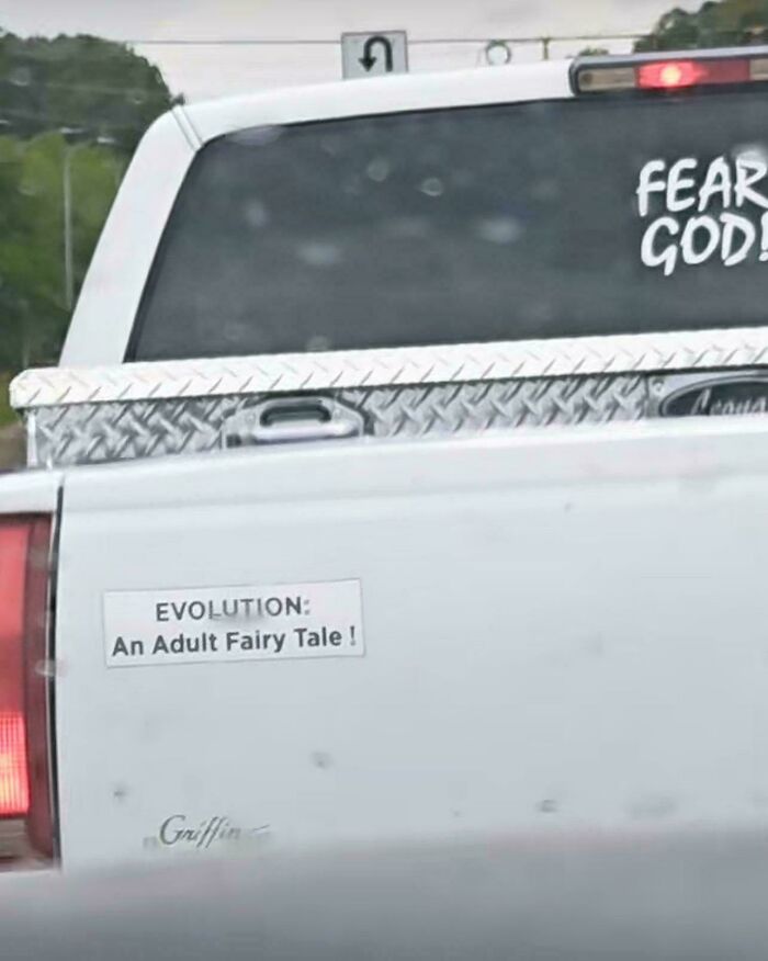 Controversial bumper stickers on a white truck reading EVOLUTION: An Adult Fairy Tale!