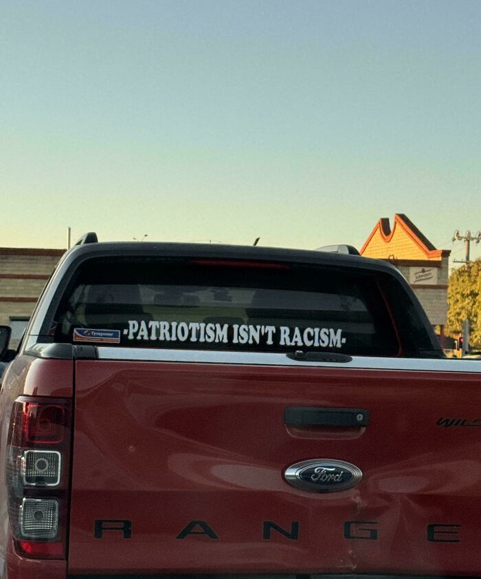 Wild bumper stickers on a red pickup truck reading Patriotism Isn't Racism on the rear windshield.
