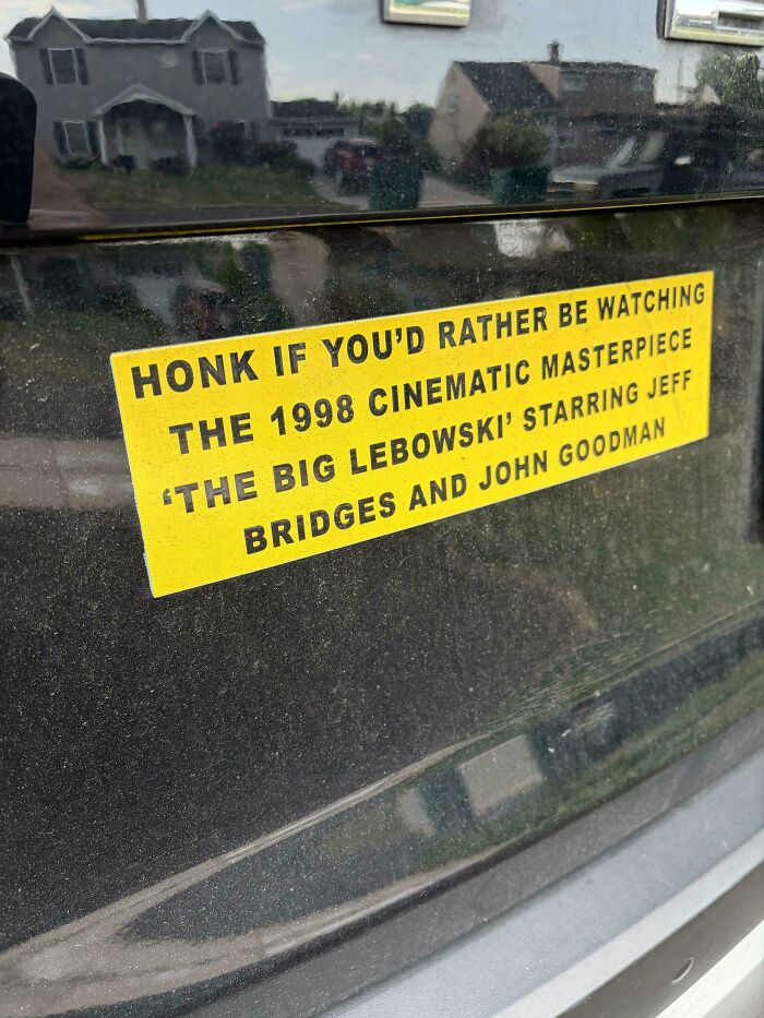A yellow bumper sticker about The Big Lebowski movie on a car rear window.