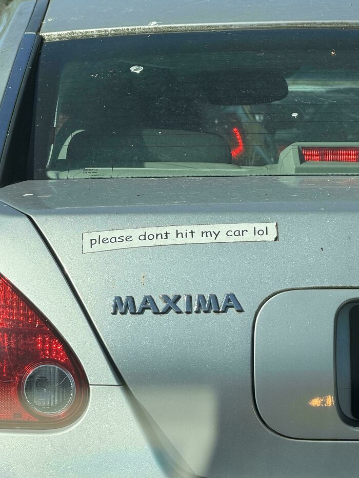A silver vehicle displaying a wild bumper sticker that reads, please dont hit my car lol, above the emblem.