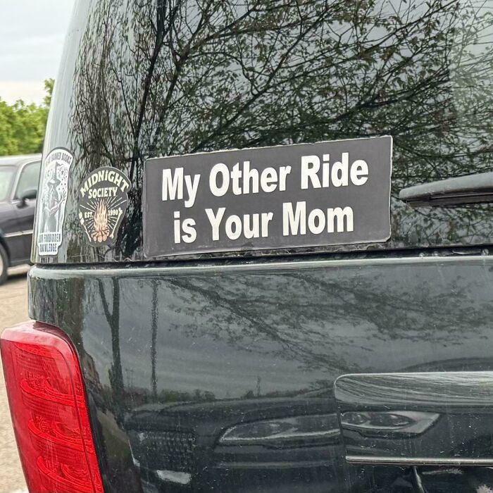 A black car rear window featuring a wild bumper sticker that says, My Other Ride is Your Mom.