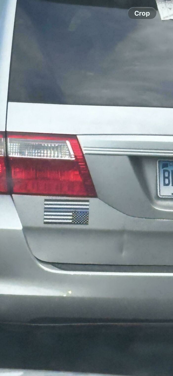 A car displaying a thin blue line American flag decal on its rear bumper next to the tail light.